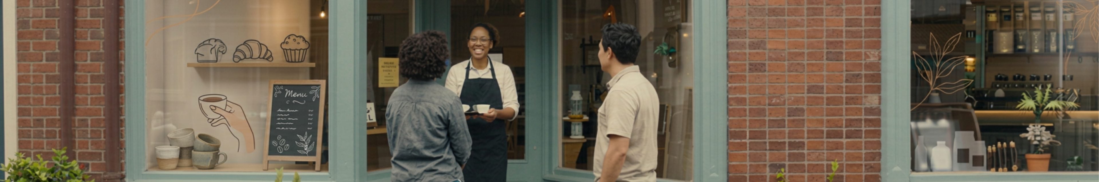 A café owner greeting customers at the door of her shop